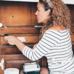 Woman at home restore old wooden cabinet painting with a roller and white pain. New refurbish