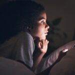 Woman, cellphone and bed in night, reading or texting for chat, blog or social media post in apartm